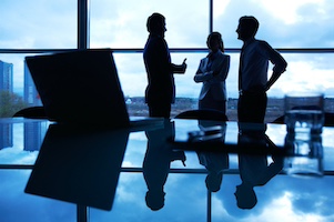 Three office workers interacting by the window with their workplace in front